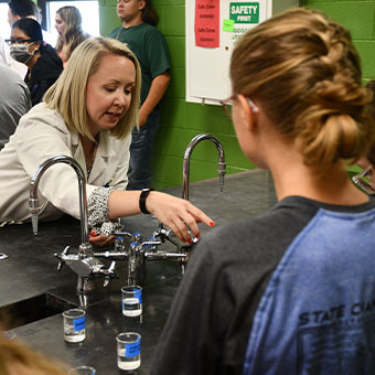 Teacher helping student in a science demonstration. Read about Beneficiary Designations Teacher helping student in a science demonstration. Read about Beneficiary Designations